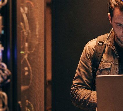 A person with a laptop beside a dark server rack
